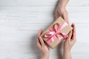 Erkek, beyaz ahşap masadaki kadına hediye paketi veriyor. Metin için boşluk