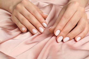 Manikürlü ellerini bej ipek kumaşta beyaz tırnak cilası ile gösteren kadın, yakın plan.