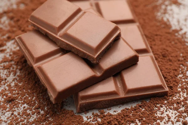 Delicious milk chocolate and cocoa powder on table, closeup