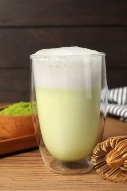 Bir bardak lezzetli matcha latte ve ahşap masada bambu çırpıcı.