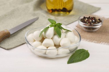 Beyaz ahşap masada lezzetli mozarella topları ve fesleğen yaprakları.