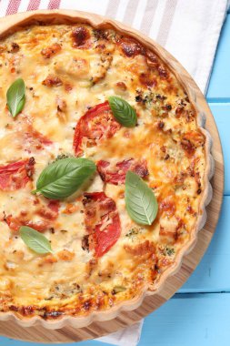 Açık mavi ahşap masada servis edilen domatesli, fesleğenli ve peynirli kiş.