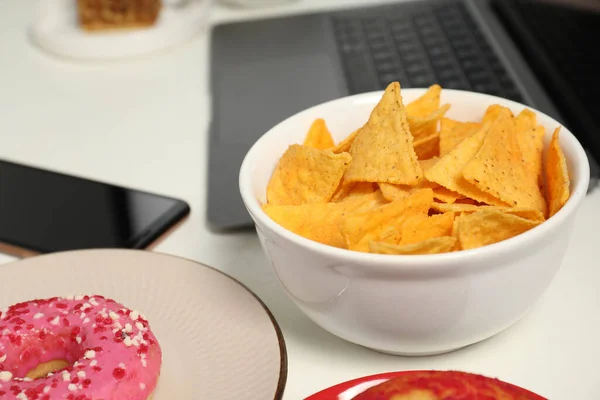 Bad eating habits at workplace. Tasty tortilla chips in bowl on white table, closeup