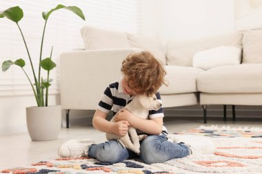 Küçük çocuk evde halıda sevimli köpek yavrusuna sarılıyor.