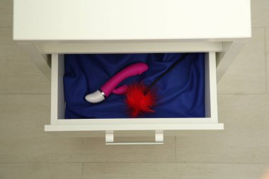 Vibratör ve tüy gıdıklayıcı kapalı çekmecede, üst manzara. Seks oyuncakları