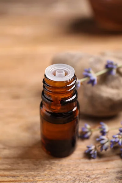 Bottle of essential oil and lavender flowers on wooden table, closeup
