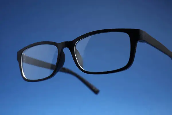 Stylish pair of glasses with black frame on blue background, closeup