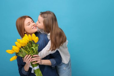 Anne ve güzel kızı açık mavi arka planda sarı lalelerle dolu bir buketle. Metin için boşluk