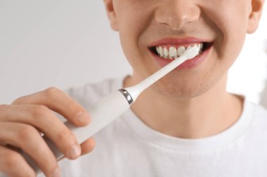 Adamın biri arka planda elektrikli diş fırçasıyla dişlerini fırçalıyor.