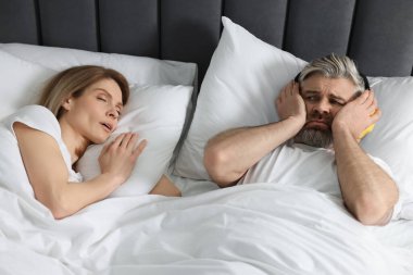 Evde yatakta horlayan karısının yanında kulaklıkları olan sinirli bir adam.