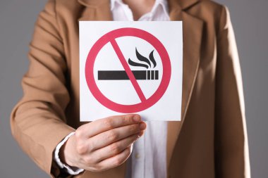 Gri arka planda sigara içilmeyen kart tutan kadın, yakın plan.