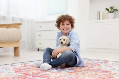 Evdeki halıda sevimli köpek yavrusu olan küçük çocuk.