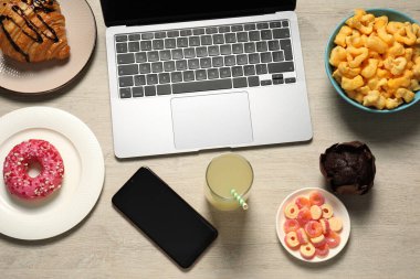 İş yerinde kötü yeme alışkanlıkları. Laptop, akıllı telefon ve ahşap masada farklı atıştırmalıklar.