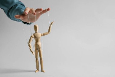Woman pulling strings of puppet on light grey background, closeup. Space for text
