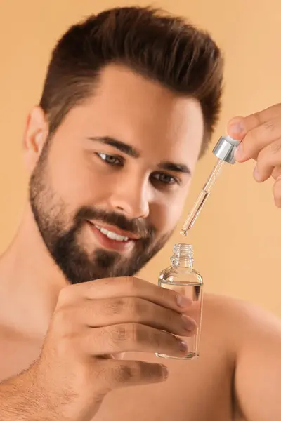 Handsome man with cosmetic serum in hands on beige background, selective focus