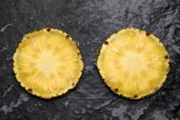 Slices of tasty ripe pineapple on black textured table, flat lay
