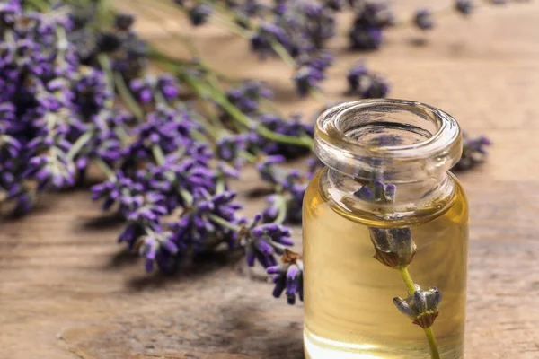 Bottle of essential oil and lavender flowers on wooden table, closeup. Space for text