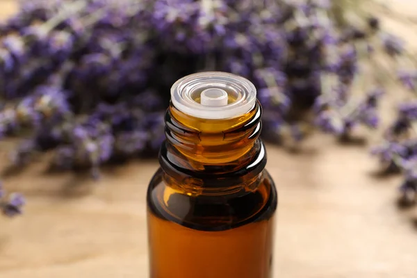 Bottle of essential oil and lavender flowers on table, closeup