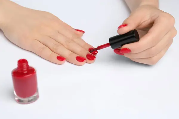 Woman painting nails with red polish on white background, closeup