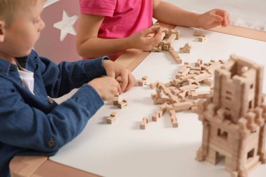 Küçük çocuk ve kız kapalı bir masada tahta kuleyle oynuyorlar, yakın plan. Çocuk oyuncağı.