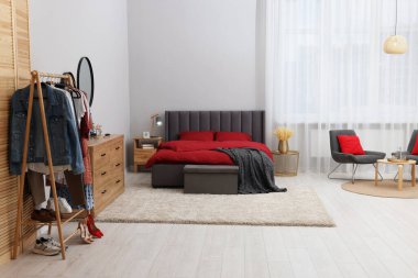 Rahat yataklı şık bir yatak odası, ahşap çekmeceler ve elbise askısı. İç tasarım