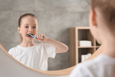 Banyoda aynanın yanında dişlerini plastik diş fırçasıyla fırçalayan tatlı küçük kız.