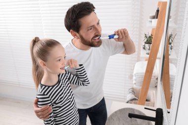 Babası ve kızı banyoda aynanın yanında dişlerini fırçalıyorlar.
