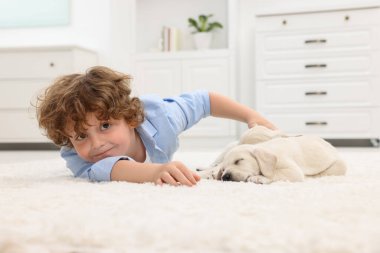 Evdeki beyaz halıda sevimli köpek yavrularıyla uzanan küçük çocuk.