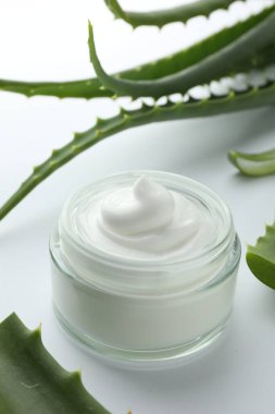 Beyaz arka planda doğal krema ve aloe yaprakları kavanozu, yakın plan.