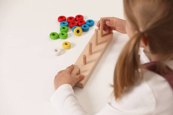 Little girl playing with stacking and counting game at white table indoors, closeup. Child's toy