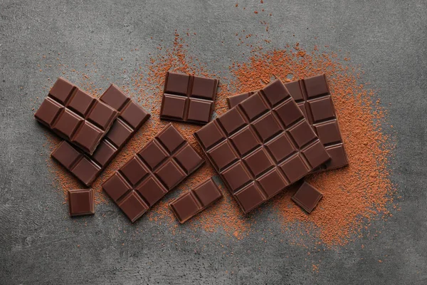 Delicious dark chocolate and cocoa powder on grey table, flat lay
