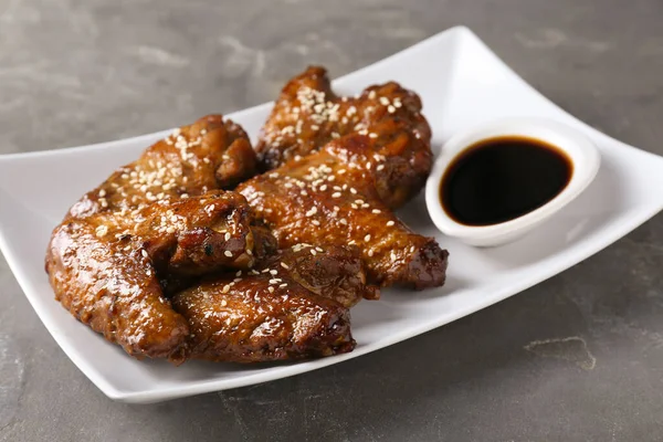 Glazed chicken wings and soy sauce on grey table, closeup