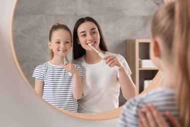 Anne ve kızı banyoda aynanın yanında dişlerini fırçalıyorlar.