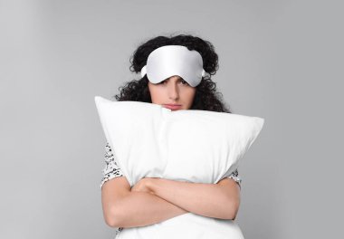 Açık gri arka planda uyku maskesi ve yastığı olan yorgun genç bir kadın. Uykusuzluk sorunu