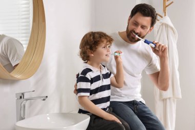 Baba ve oğlu banyoda dişlerini fırçalıyorlar.