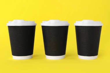 Sarı arka planda beyaz kapaklı kağıt bardaklar. Kahve hazır.