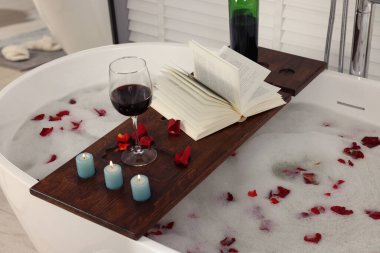 İçinde şarap, kitap, yanan mumlar ve küvette gül yaprakları olan ahşap tahta bir tahta.