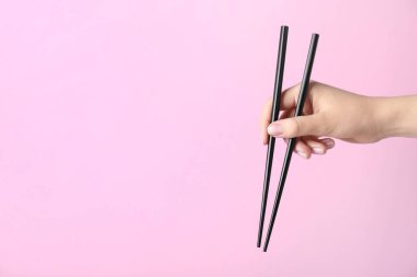 Pembe arka planda bir çift siyah çubuk tutan kadın, yakın plan. Metin için boşluk