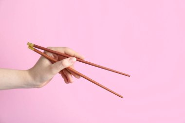 Pembe arka planda bir çift tahta çubuk tutan kadın, yakın plan.