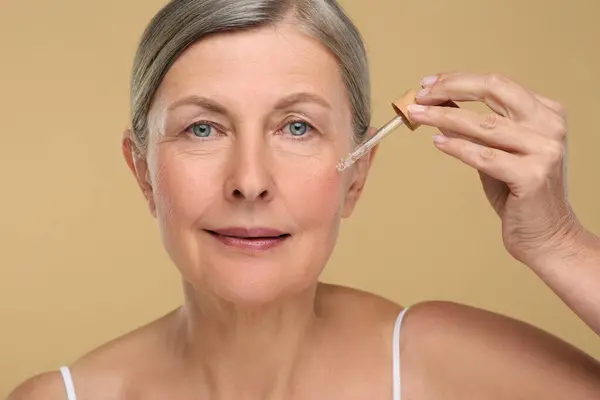 Seniorin Trägt Kosmetikprodukt Auf Ihre Alternde Haut Vor Beigem Hintergrund — Stockfoto