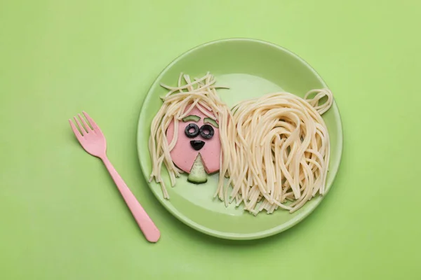 Creative serving for kids. Plate with cute dog made of tasty pasta, sausage and cucumber on green table, flat lay