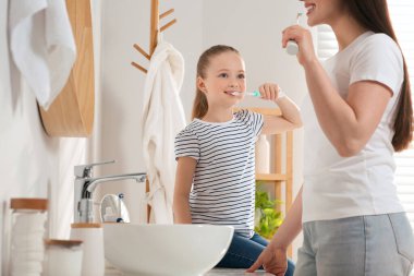 Anne ve kızı banyoda dişlerini fırçalıyorlar.