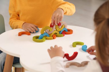 Küçük çocuklar, beyaz masada renkli ahşap parçalarla oynuyorlar, yakın plan. Geliştirme oyuncağı