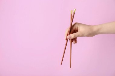 Pembe arka planda bir çift tahta çubuk tutan kadın, yakın plan. Metin için boşluk