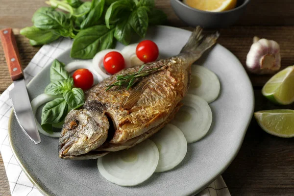 Delicious dorado fish with vegetables and herbs served on wooden table, closeup