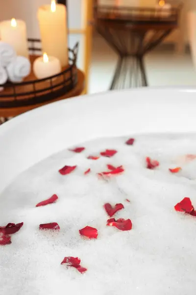 Foam and red rose petals in bath tub, closeup