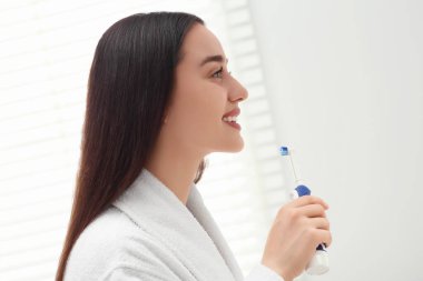 Banyoda dişlerini elektrikli diş fırçasıyla fırçalayan genç bir kadın.