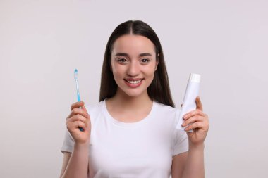 Beyaz arka planda plastik diş fırçası ve tüp diş macunu tutan mutlu kadın.