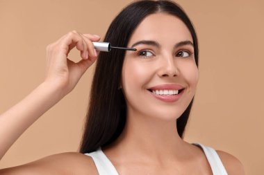 Kirpiklerine bej arka planda serum süren güzel bir kadın. Kozmetik ürünü