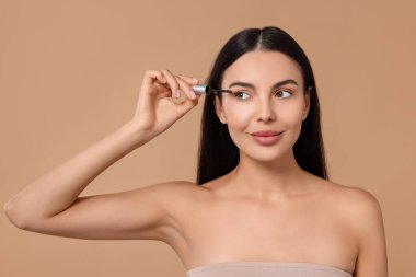 Kirpiklerine bej arka planda serum süren güzel bir kadın. Kozmetik ürünü